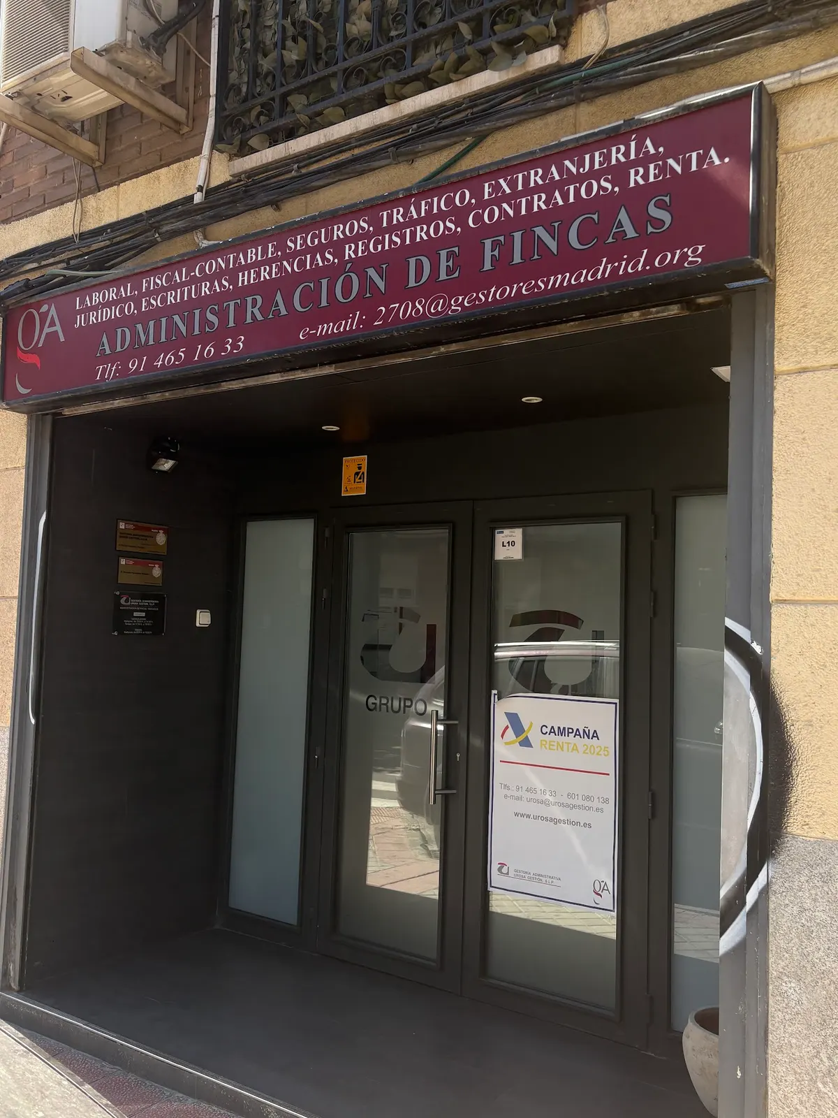 Entrada de Urosa Gestión en la calle Juana Urosa: rótulo granate con los servicios de la gestoría y puertas de cristal con la U del logotipo
