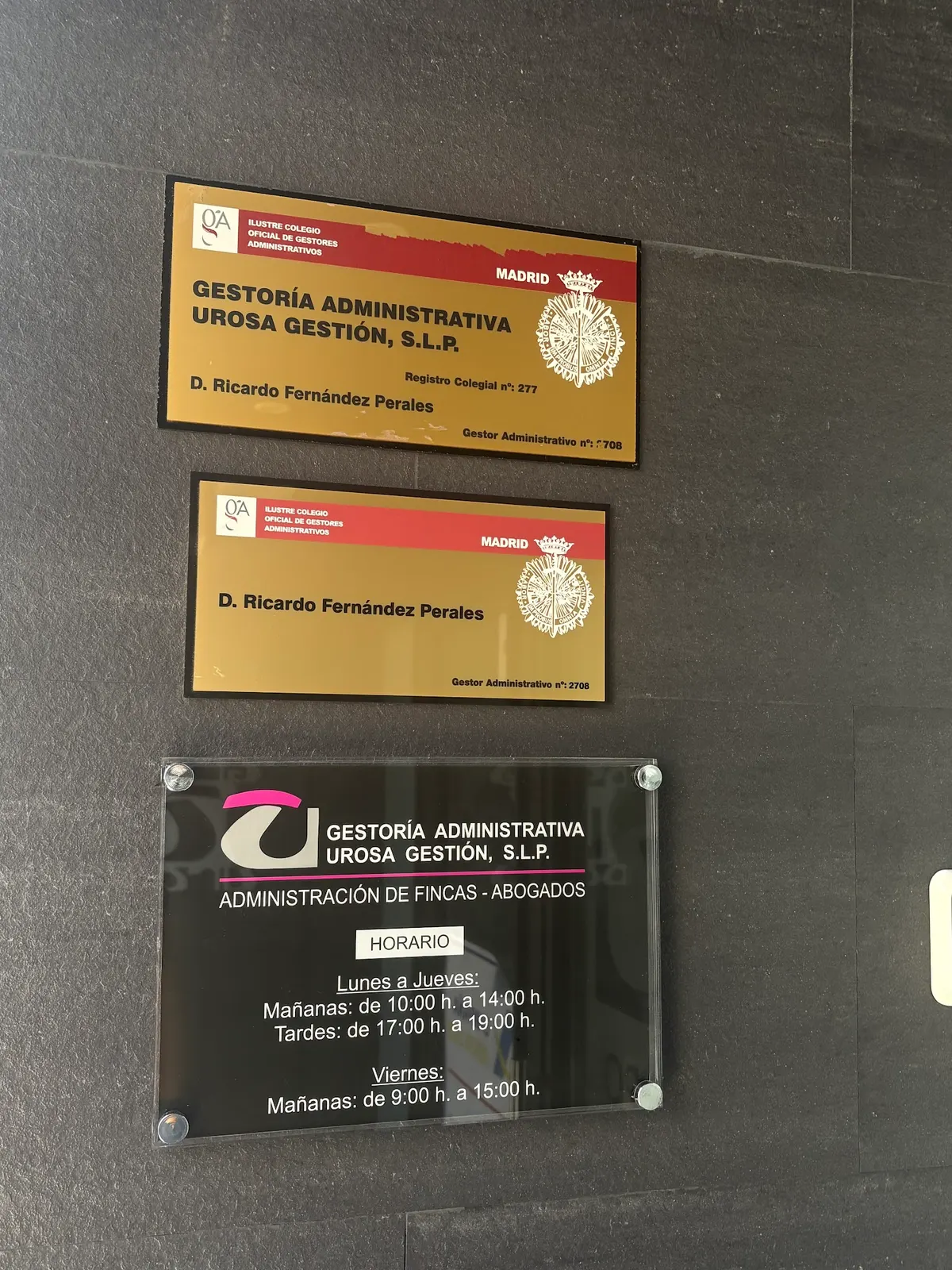 Placas del Colegio Oficial de Gestores Administrativos de Madrid y placa con el horario de Urosa Gestión en la pared de la entrada